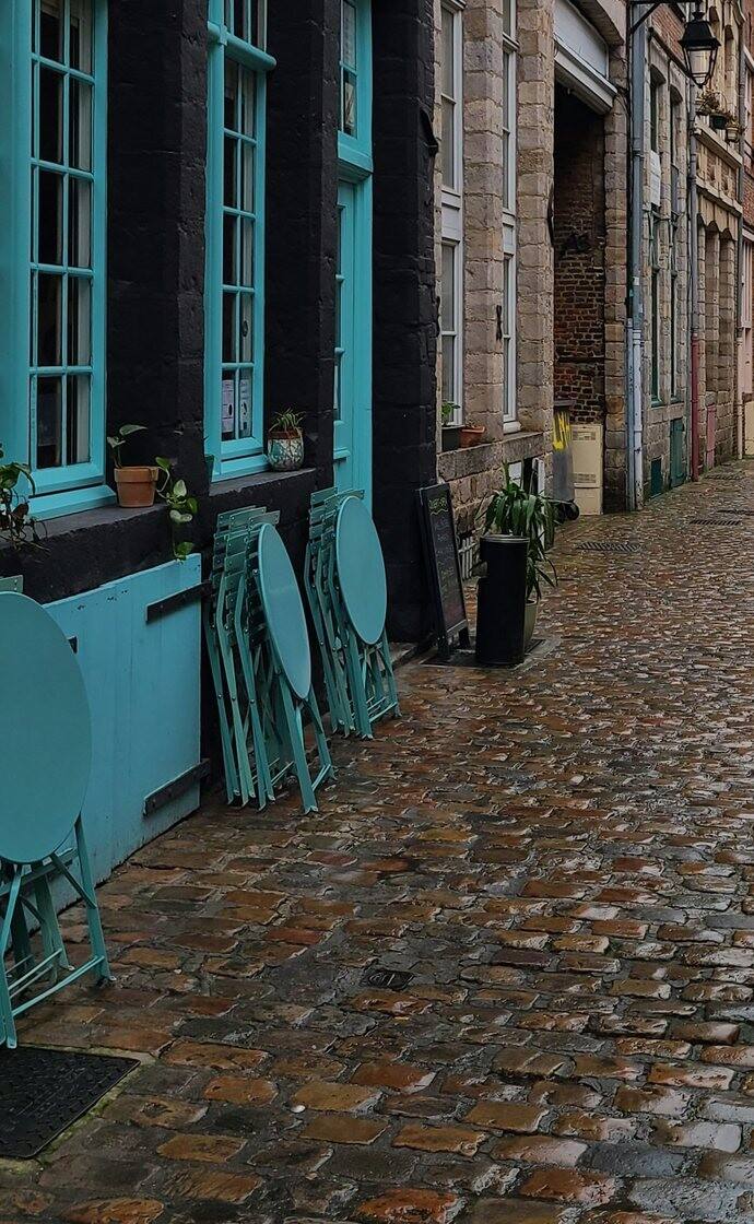 Des tables pliées devant une devanture turquoise, sur les pavés mouillés du Vieux-Lille.
